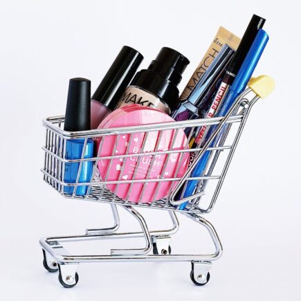 Miniature shopping cart filled with a variety of cosmetics on a white background.